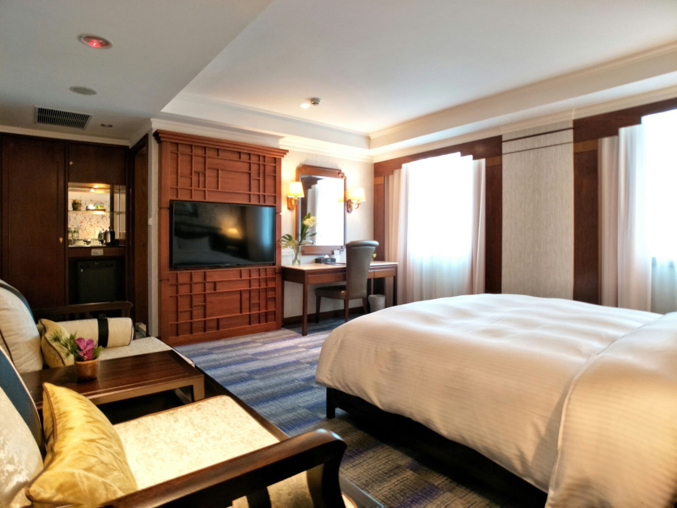 Una habitación de hotel con una cama grande, un escritorio con una silla, un televisor y una zona de estar con sofá y sillón.