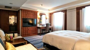 Una habitación de hotel con una cama grande, un escritorio con una silla, un televisor y una zona de estar con sofá y sillón.