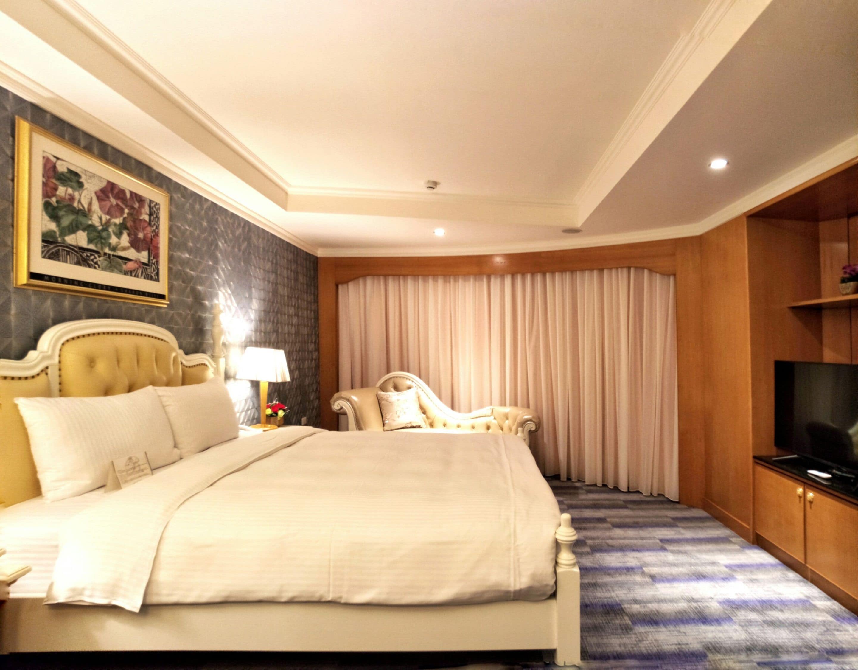 A hotel room with a large bed, a desk, a chair, a television, and a painting on the wall.