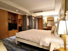 Una habitación de hotel con una cama grande, un armario de madera, televisión y un escritorio con lámpara.