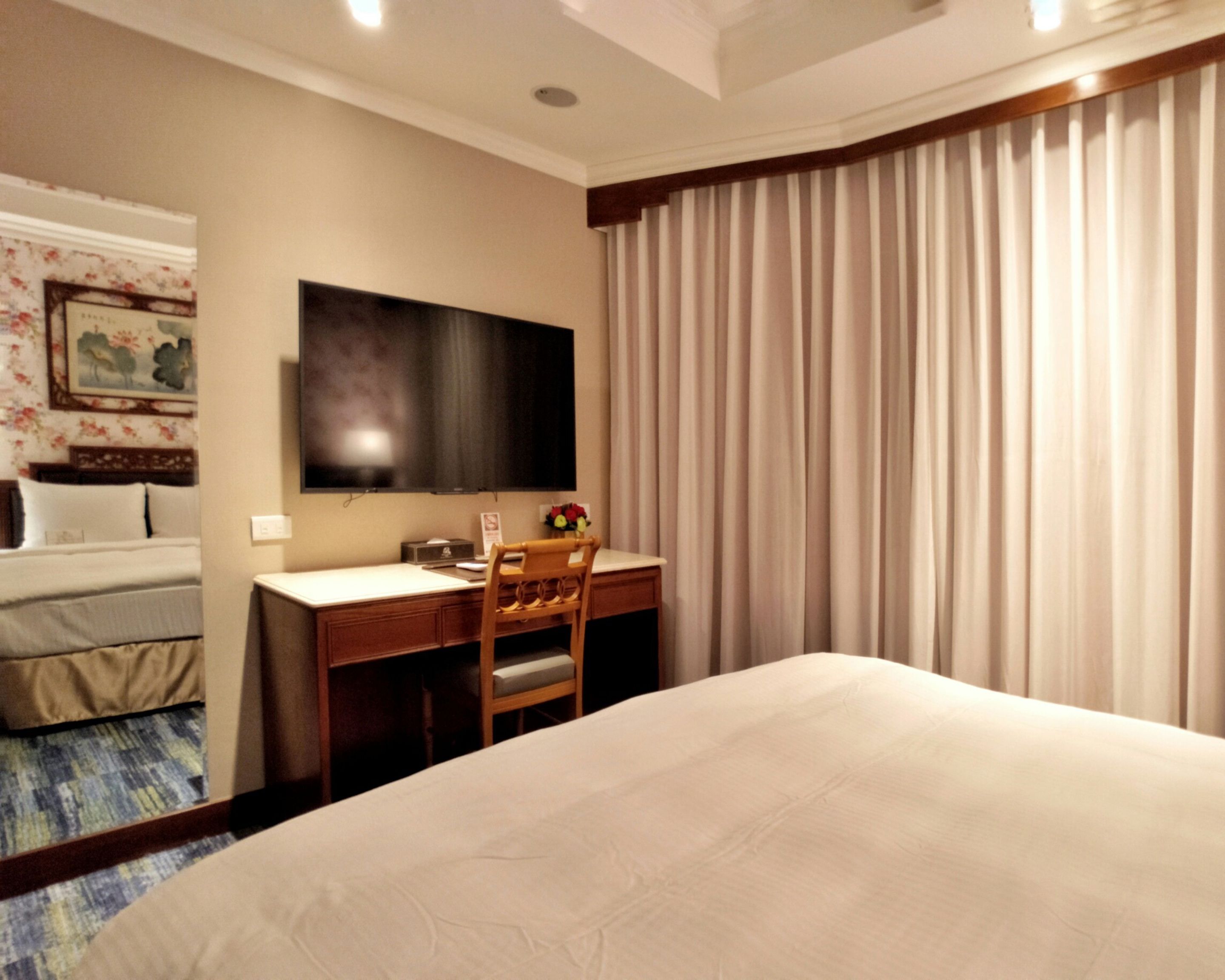 Hotelkamer met een bed, een bureau met stoel, een flatscreen televisie en een groot raam met gordijnen.