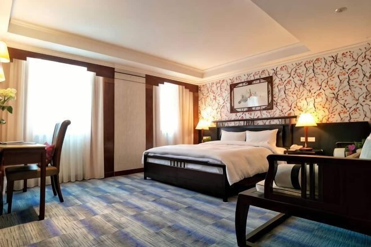 A hotel room with a bed, desk, chair, and a large window.