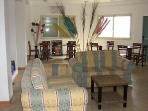 A living room with a sofa set, a coffee table, and chairs. There is a dining area with a table and chairs in the background.