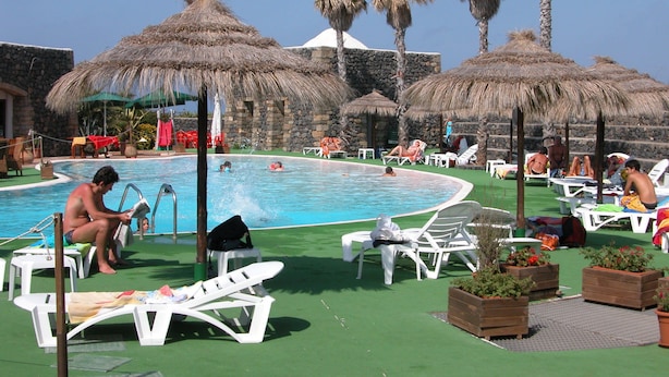 A pool area with lounge chairs, umbrellas, and palm trees.