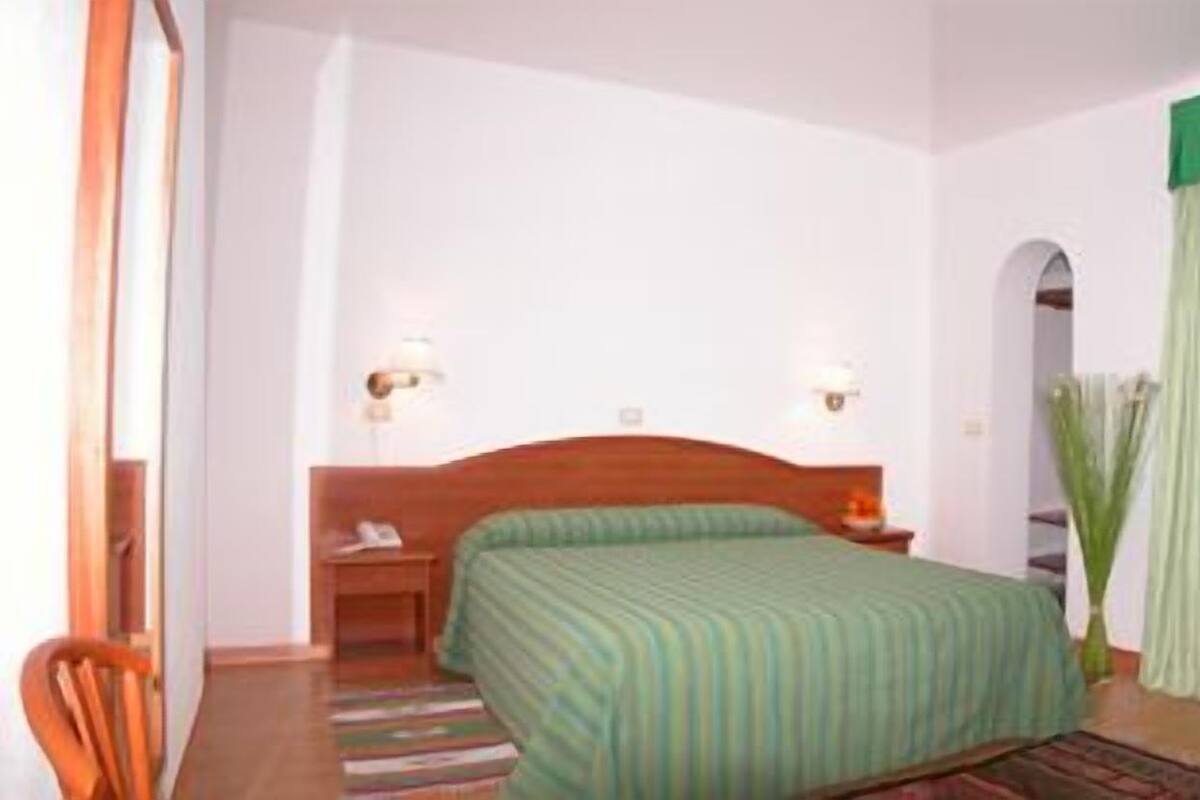 Ein Hotelzimmer mit einem Einzelbett, einem Nachttisch, einem Stuhl und einem grünen Vorhang.