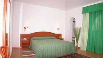Een hotelkamer met een enkel bed, een nachtkastje, een stoel en een groen gordijn.
