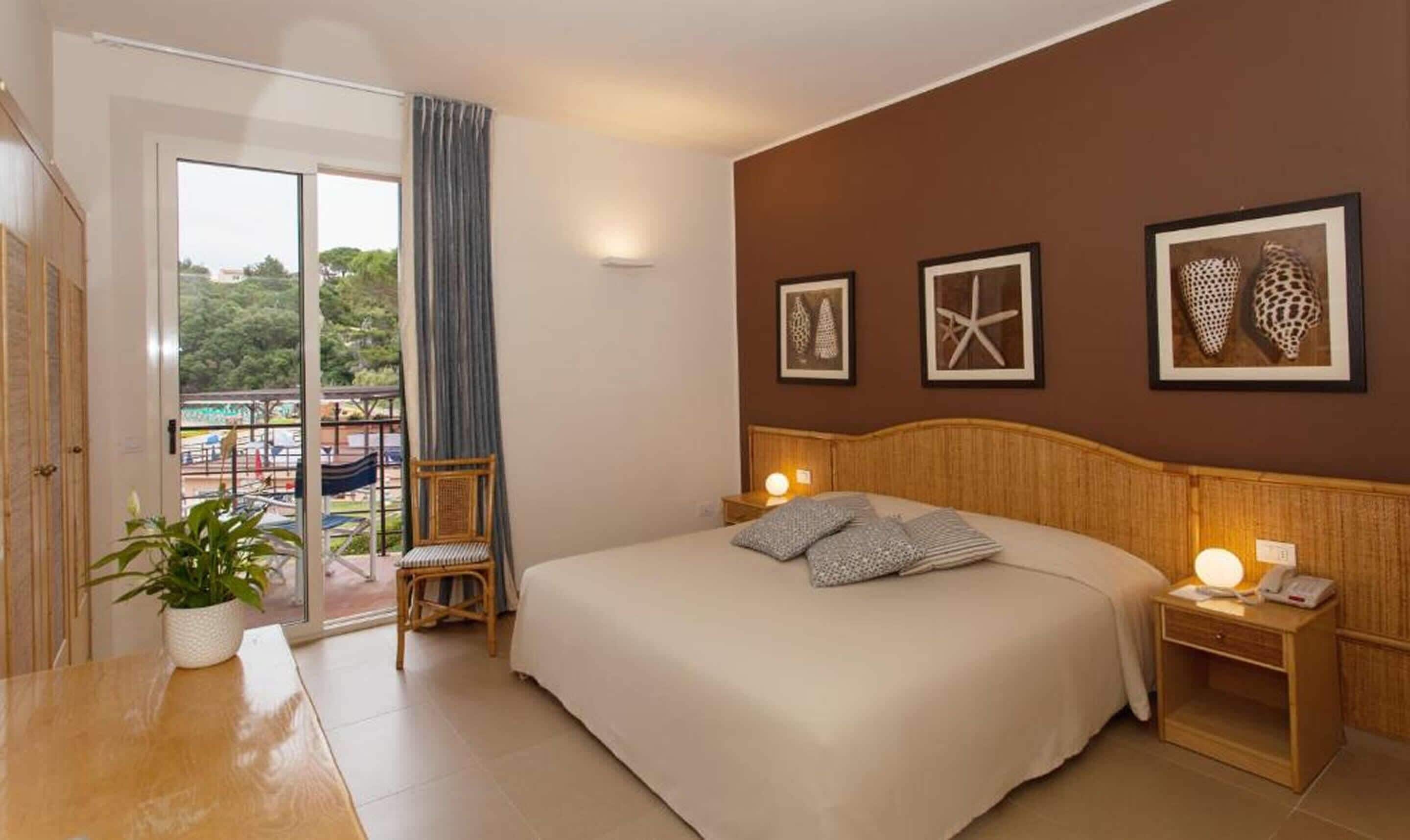 Un dormitorio con una cama grande, una mesita de noche, una silla, una planta en maceta y un balcón con vistas.