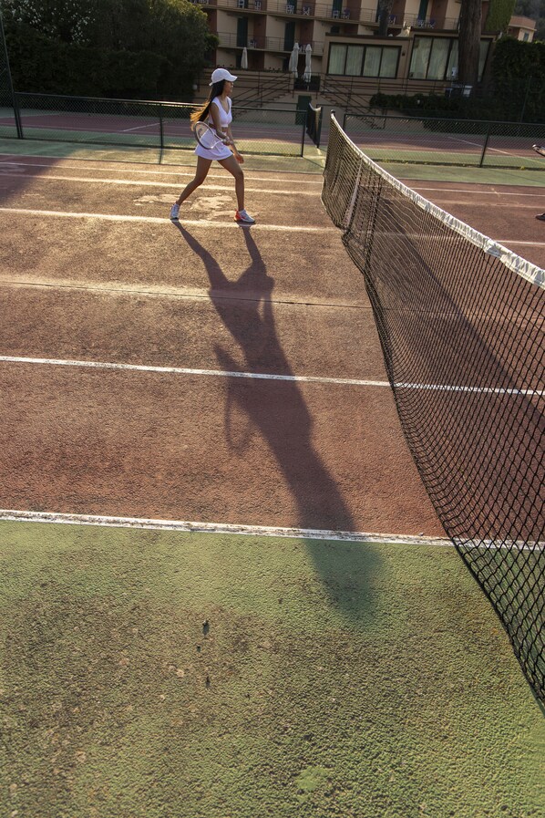 A tennis court with a net, a player in a white outfit, and a shadow of the player.