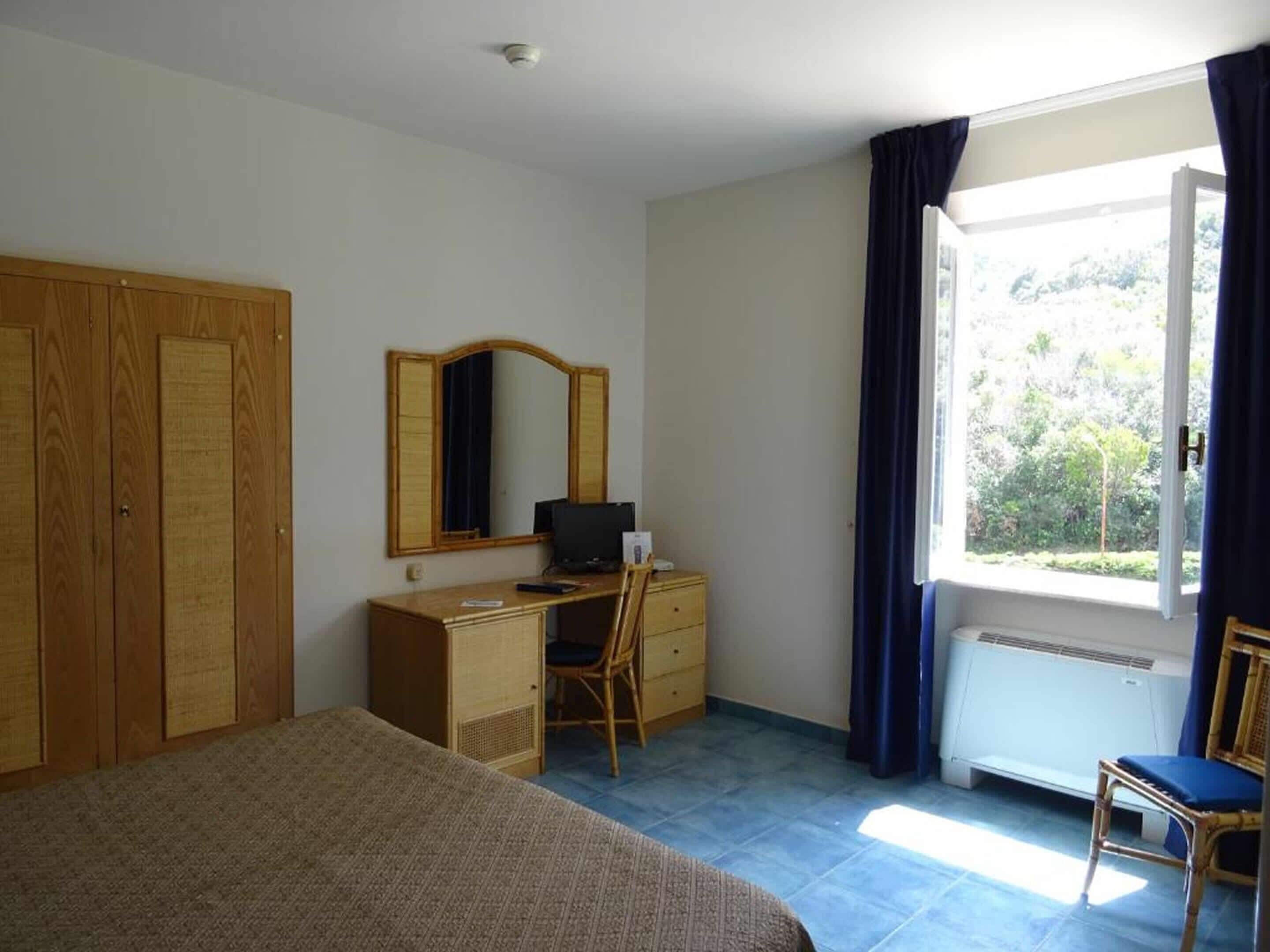 Una camera da letto con un letto, una scrivania con una sedia, un armadio, uno specchio e una finestra con tende.