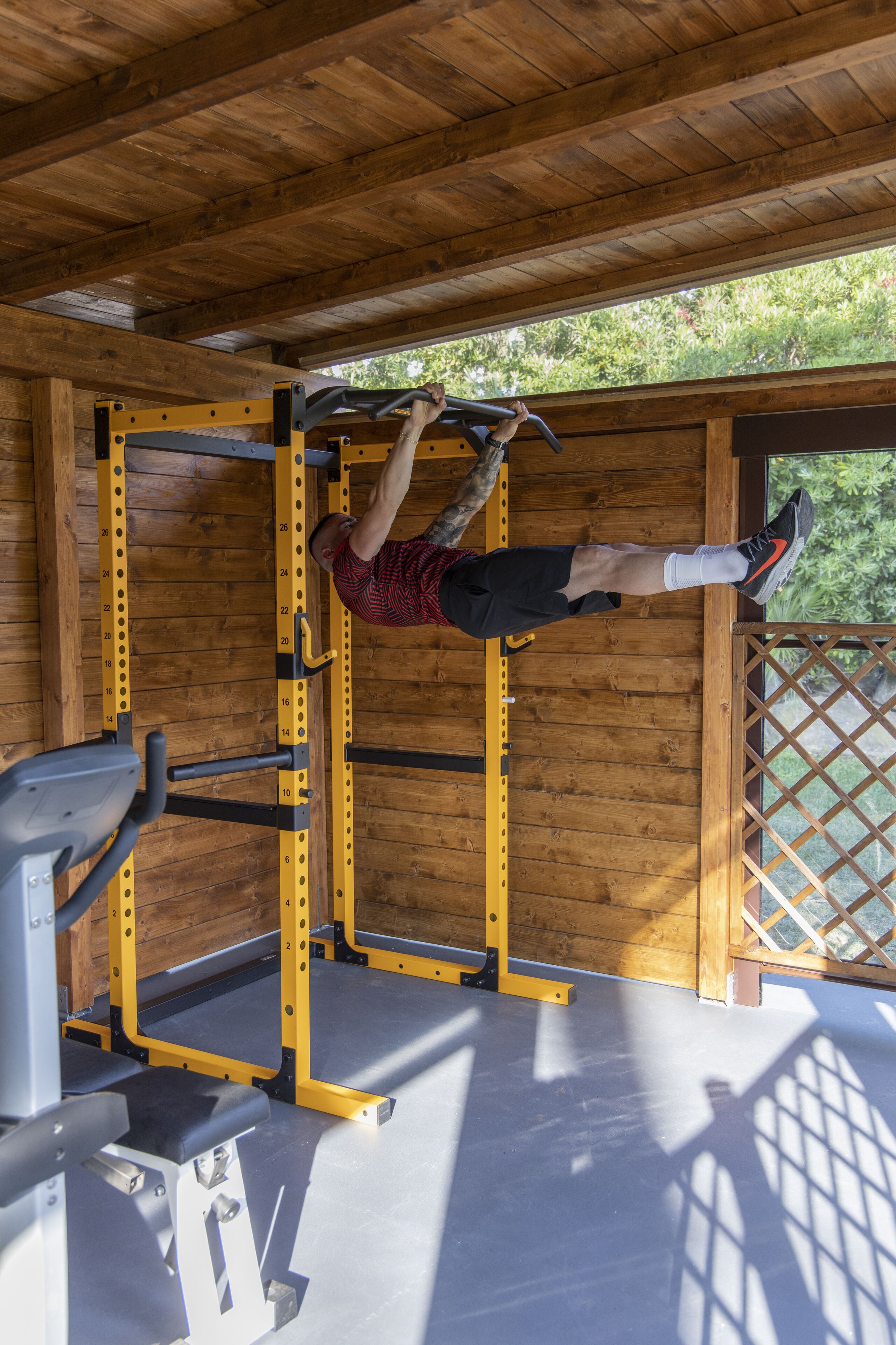 Une salle de sport équipée d’une barre de traction, d’un banc de musculation et dotée d’un plafond en bois.