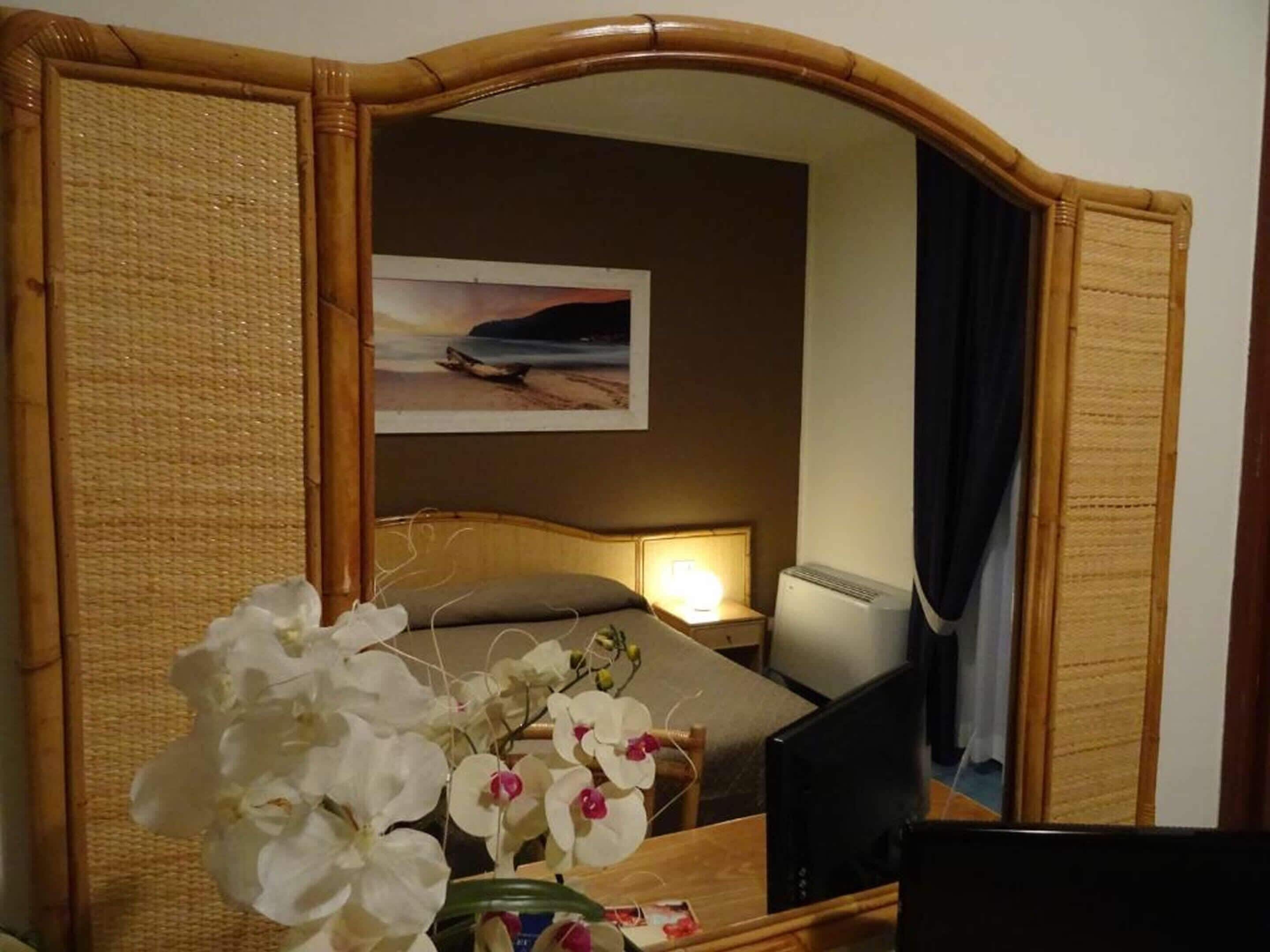 A hotel room with a bed, a bedside lamp, a TV, and a decorative orchid arrangement.
