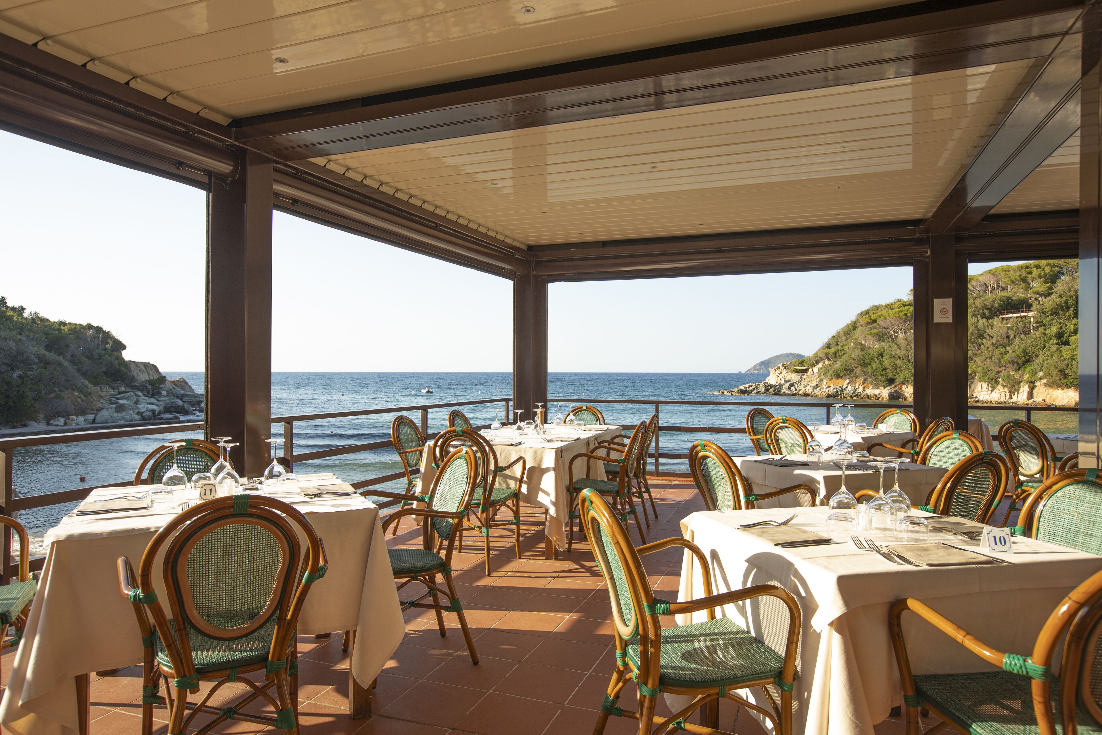 A restaurant with tables set for dining, overlooking a coastal view.
