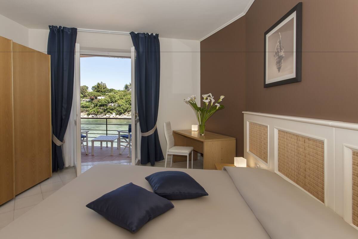 A bedroom with a bed, a desk, a chair, and a view of a balcony.