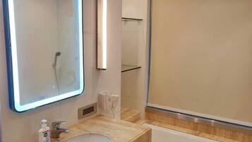 Un baño moderno con un espejo grande, un lavamanos y una bañera.