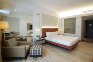 A modern hotel room with a large bed, a sofa, a small table, and a lamp.