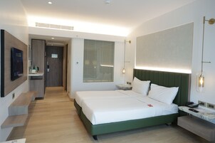 A modern hotel room with a large bed, a desk, and a bathroom visible through an open door.