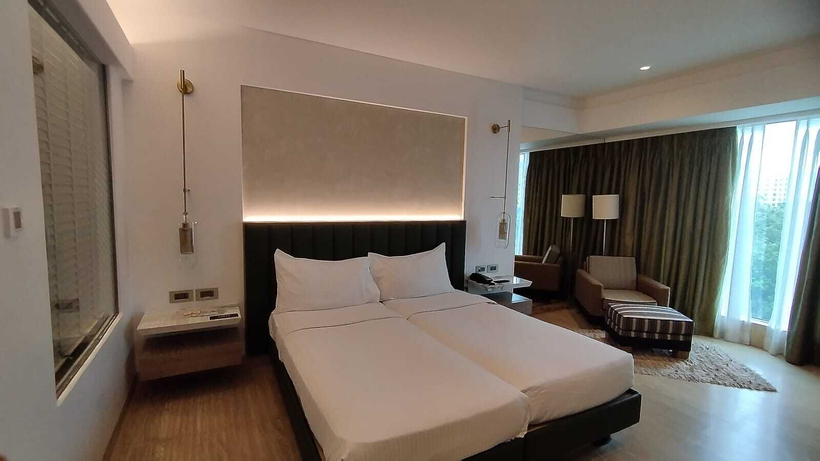 Habitación de hotel moderna con una cama grande, mesitas de noche, un escritorio, una silla y vistas al exterior.