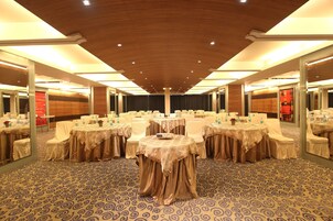 A banquet hall with round tables, chairs, and a patterned carpet.