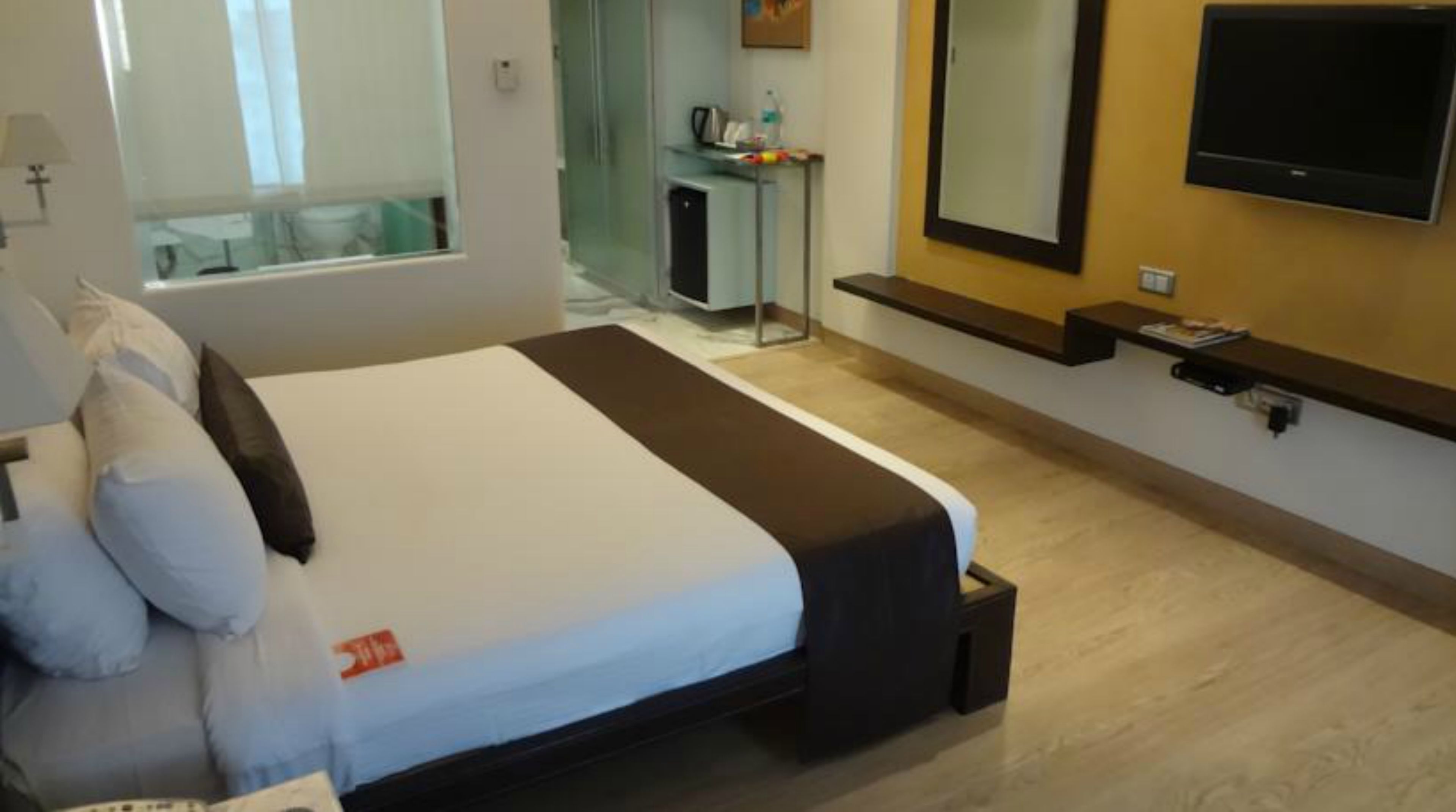A hotel room with a bed, a TV mounted on the wall, a small desk, and a mirror.