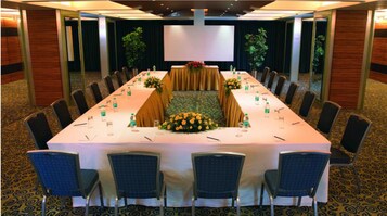 A conference room with a long table, chairs, and a stage with a screen.