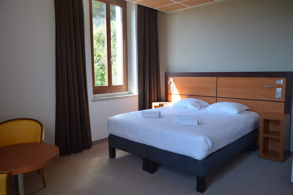 Una habitación de hotel con cama, mesita de noche, una silla y una ventana con cortinas.