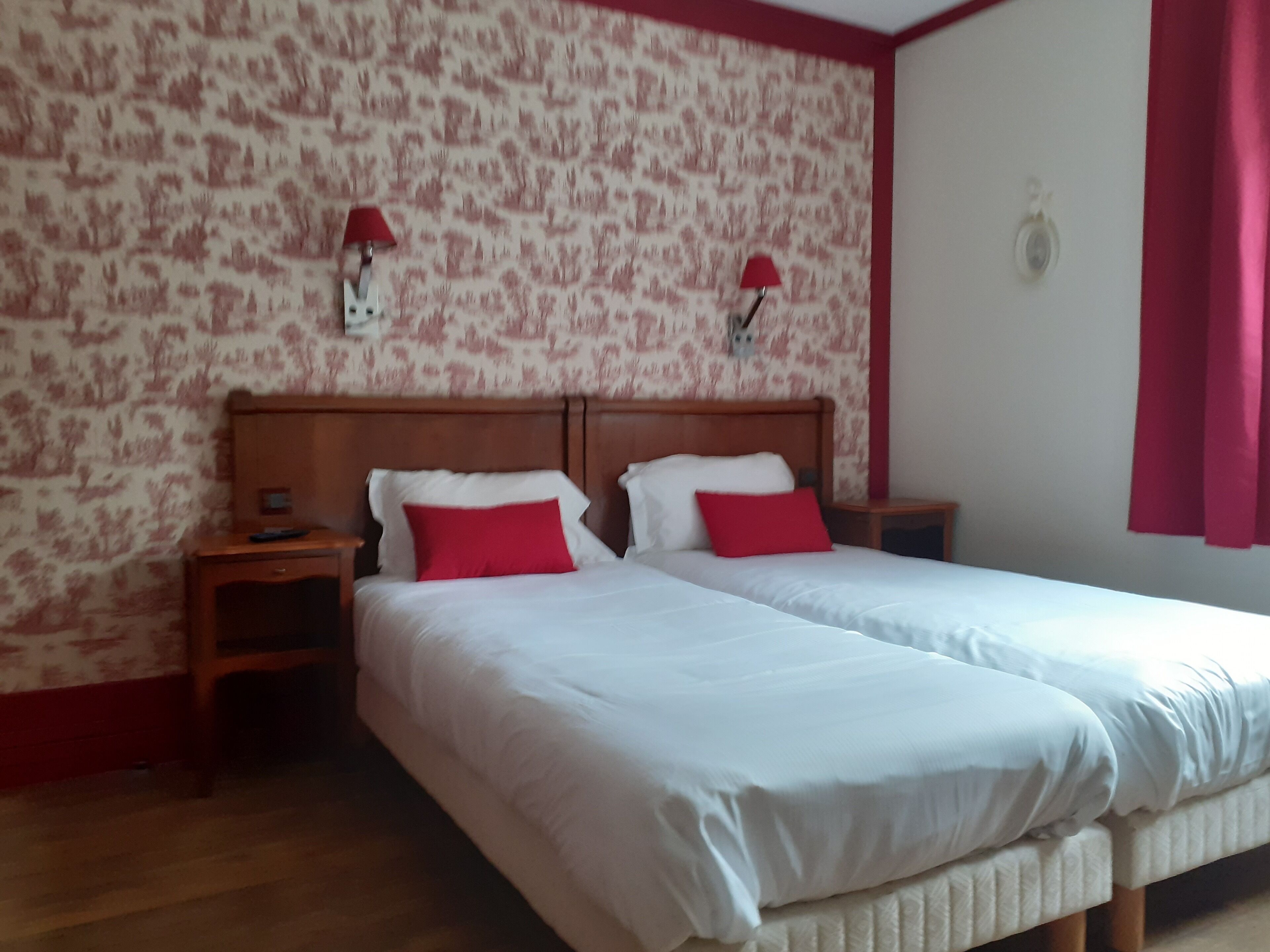 Una cama doble con ropa de cama blanca y almohadas rojas, dos mesitas de noche y un papel tapiz estampado.