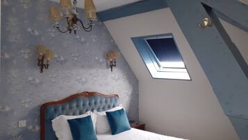 Ein Schlafzimmer mit schrägen Wänden, einem Oberlicht, einer Kristallleuchtre und einem Bett mit blau-weißer Bettwäsche.