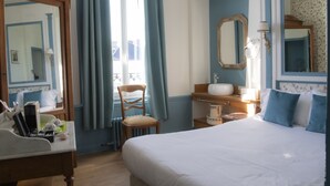 A hotel room with a bed, a chair, a desk with a lamp, a dresser, and a mirror.