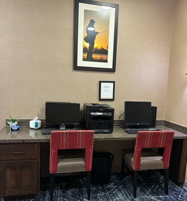 A workspace with two desks, two chairs, two monitors, a printer, and a framed picture on the wall.