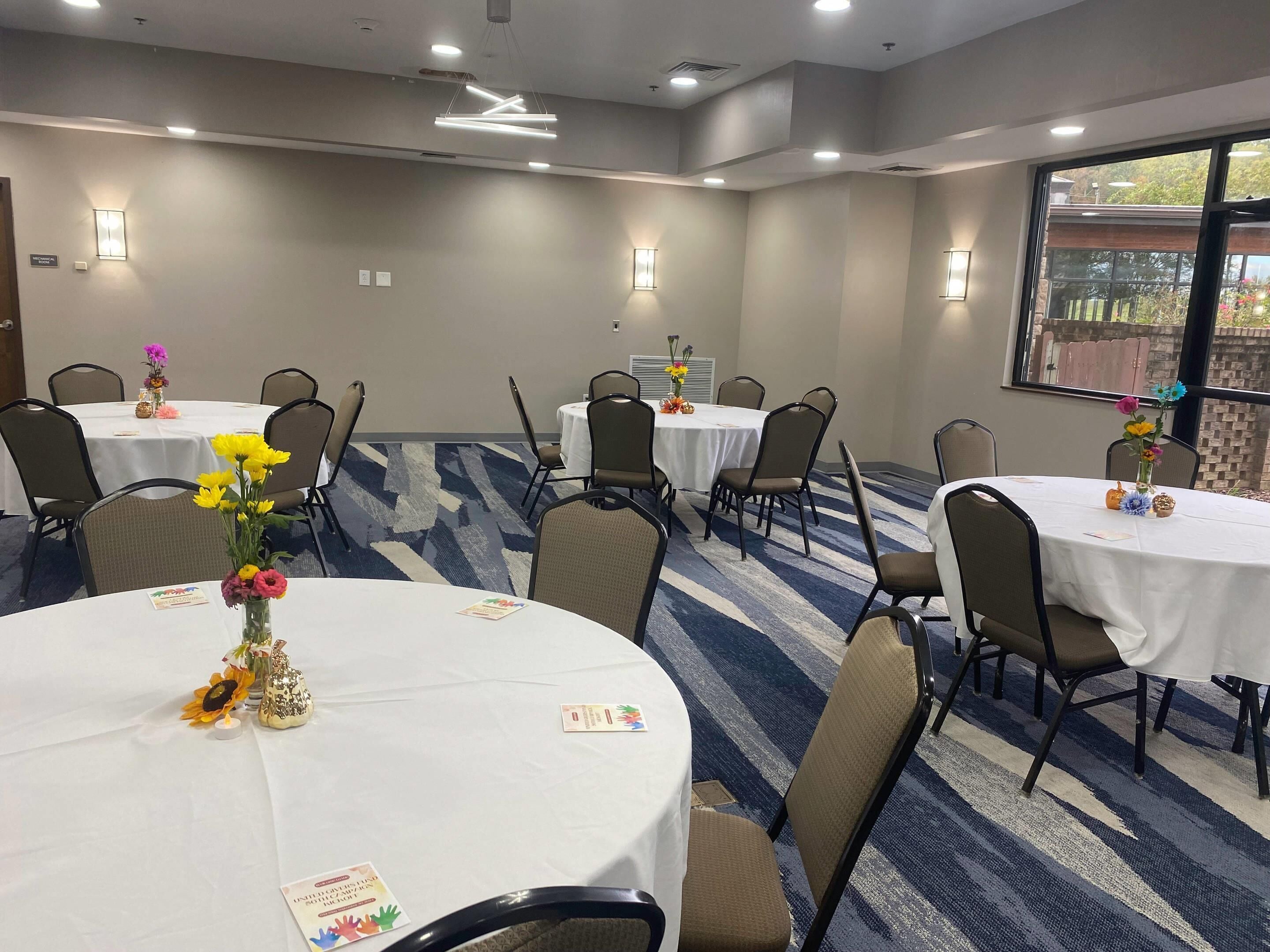 Un salón de conferencias con varias mesas, sillas y centros de mesa con flores.
