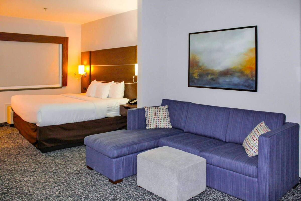 Een hotelkamer met een bed, een bank, een klein poufje, een nachtkastje en een schilderij aan de muur.