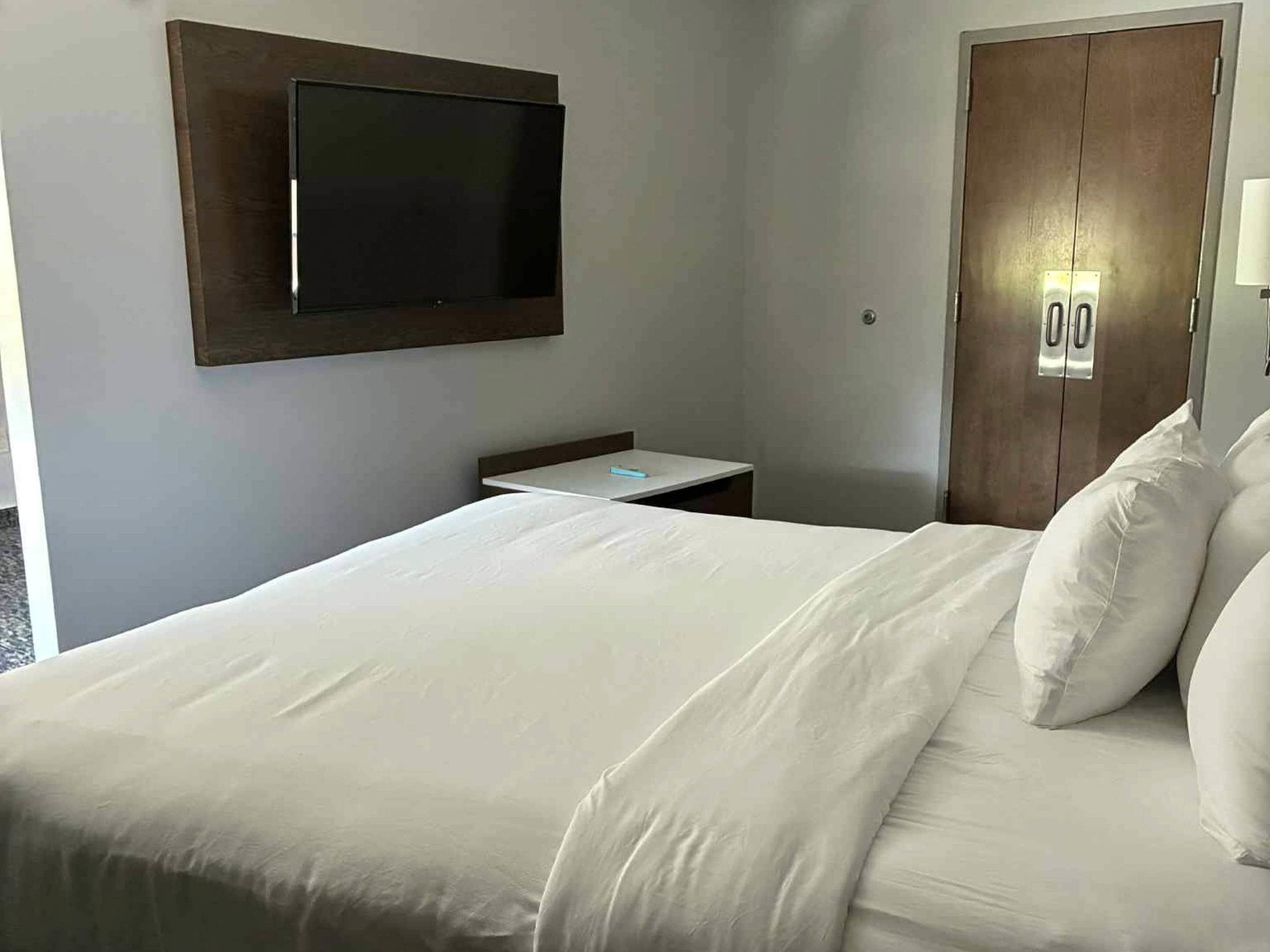 Habitación de hotel con cama, mesita de noche, televisor de pantalla plana montado en la pared y armario.