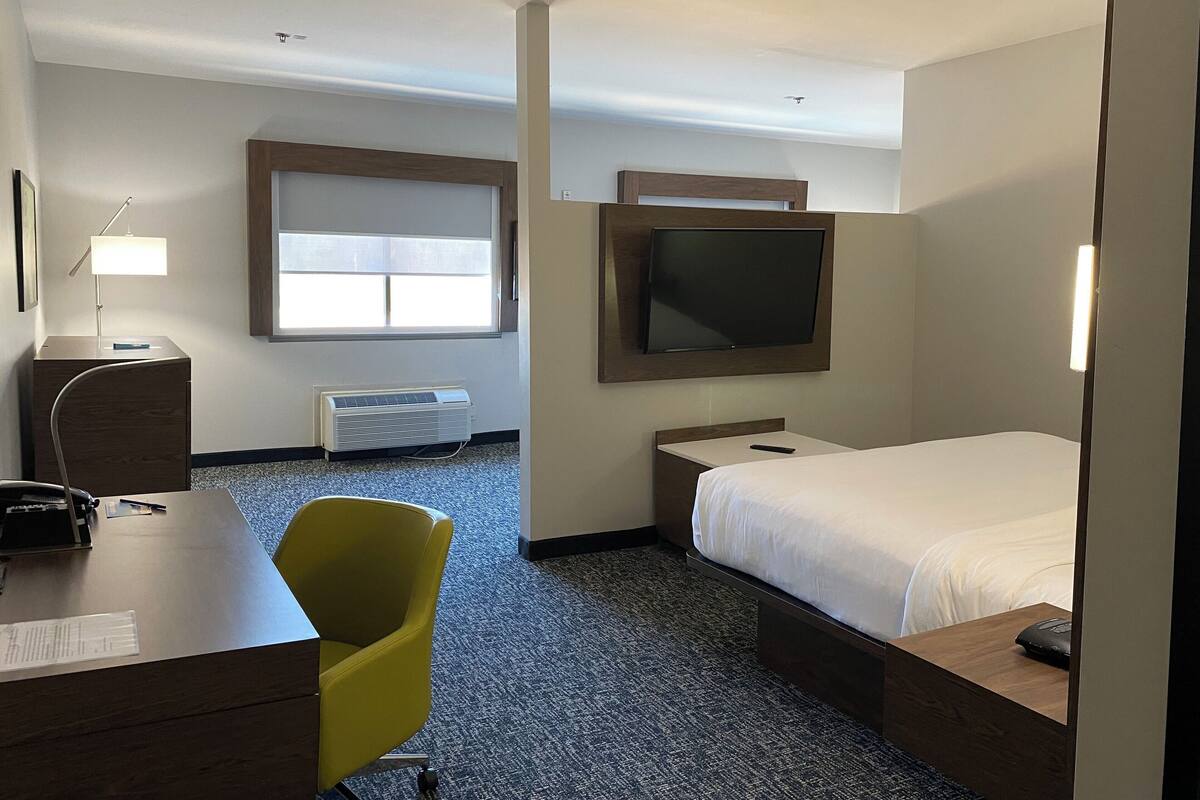 Een hotelkamer met een bed, een bureau, een stoel, een aan de muur bevestigde televisie en een raam.
