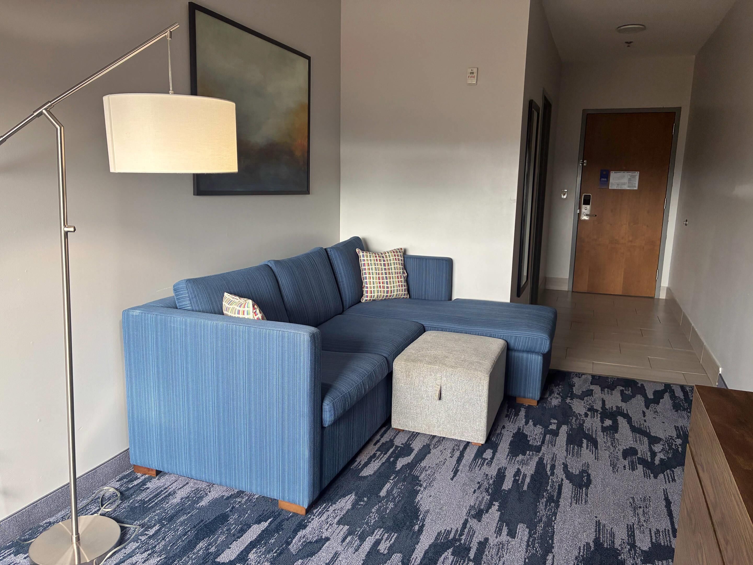 A modern living room with a blue sectional sofa, a floor lamp, a patterned rug, and a door leading to another room.