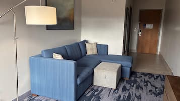 A modern living room with a blue sectional sofa, a floor lamp, a patterned rug, and a door leading to another room.