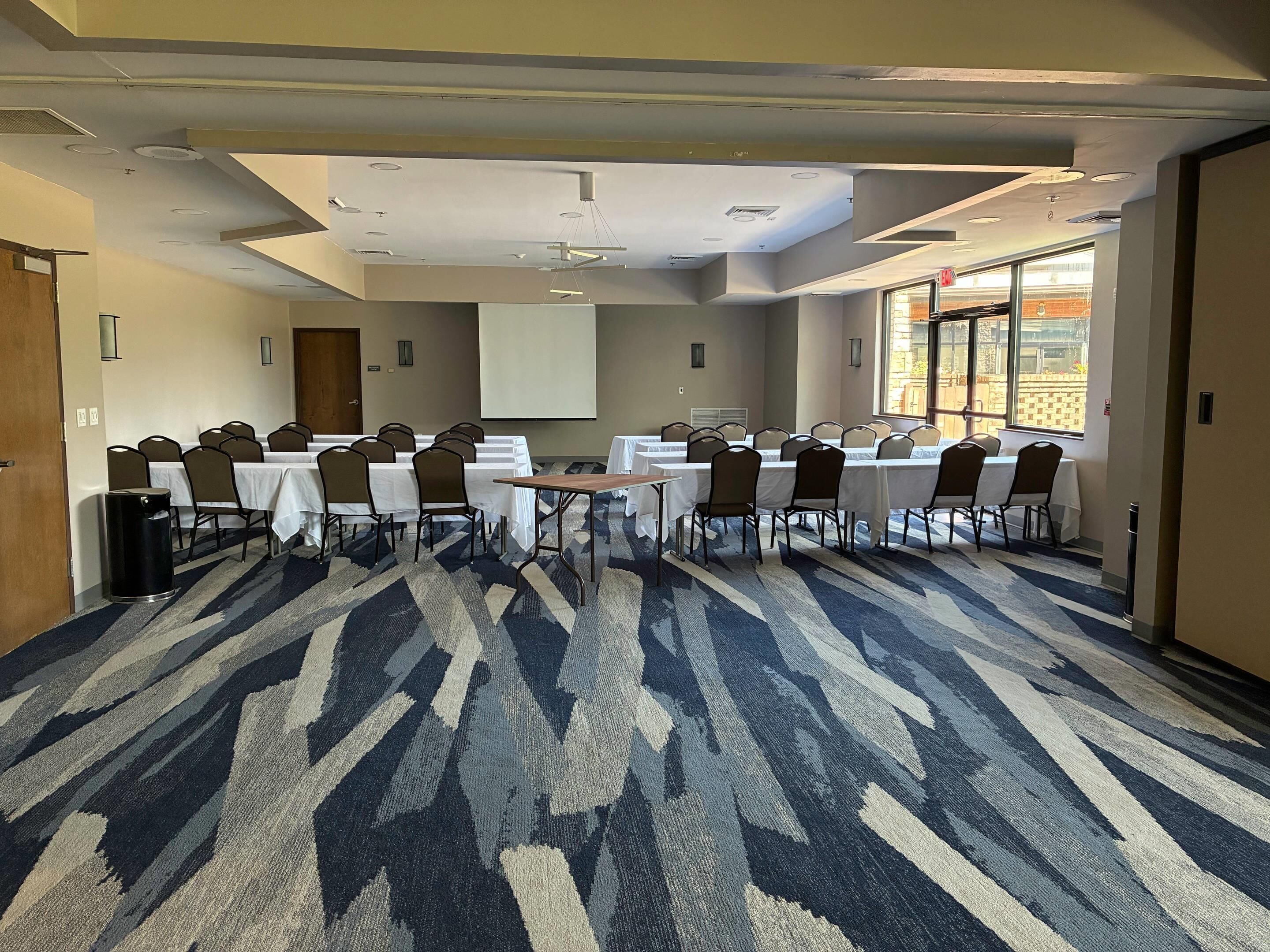 A conference room with a large screen, multiple tables, and chairs arranged for meetings.