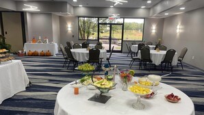 Un salón de conferencias con mesas redondas, manteles blancos y diversos alimentos sobre las mesas.