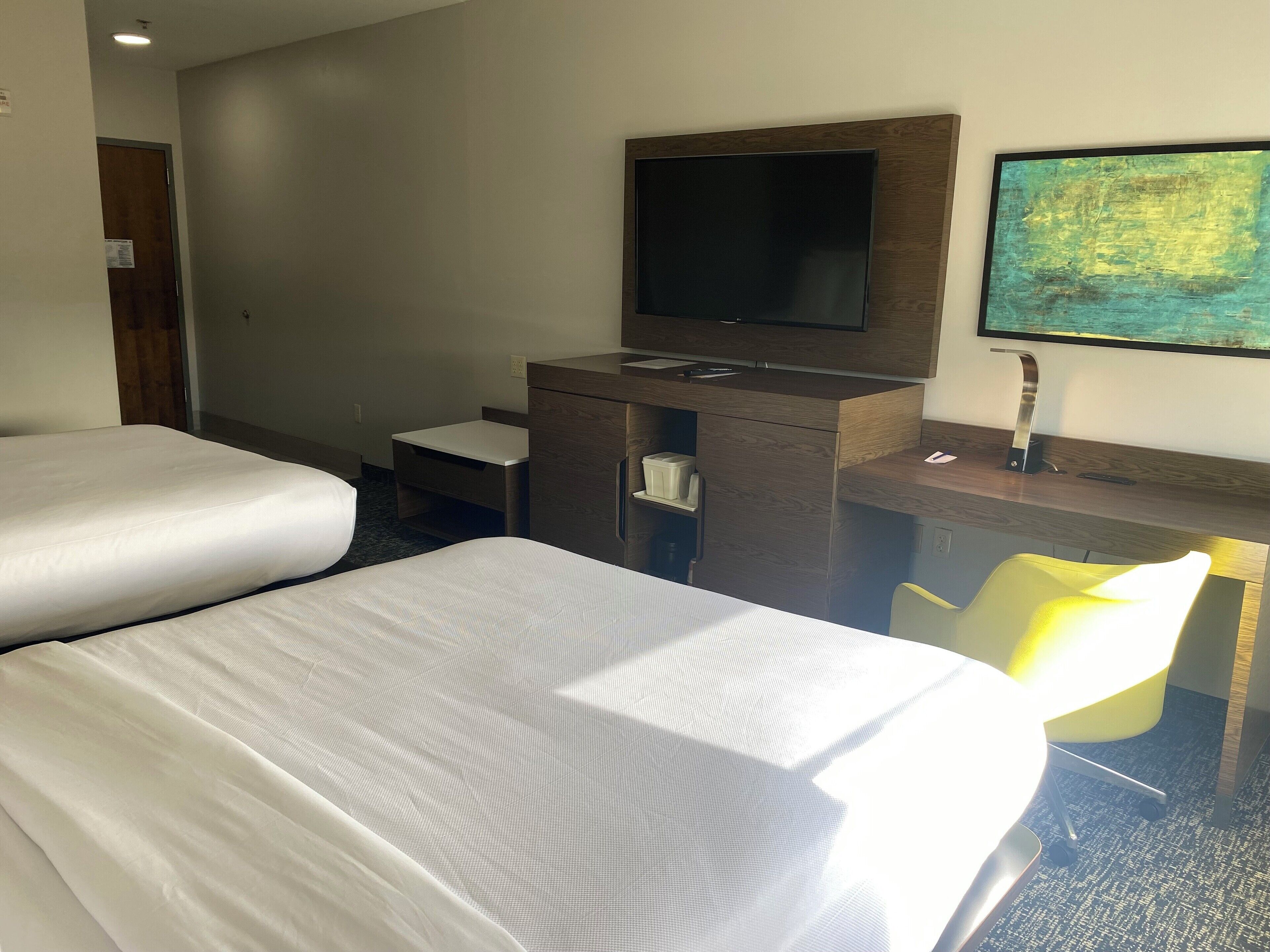 Une chambre d’hôtel avec deux lits, un bureau doté d’un téléviseur à écran plat, une petite chaise et un tableau au mur.