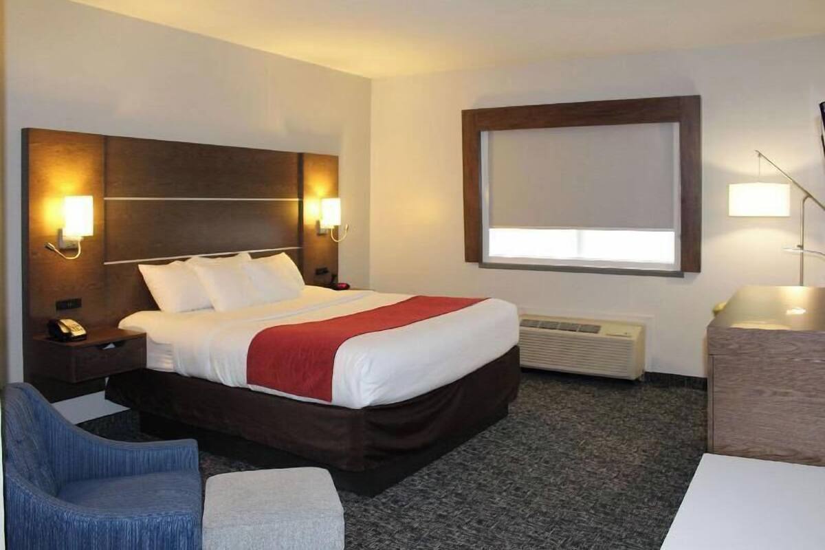 Een hotelkamer met een bed, nachtlampjes, een bureau, een stoel en een raam met zonwering.