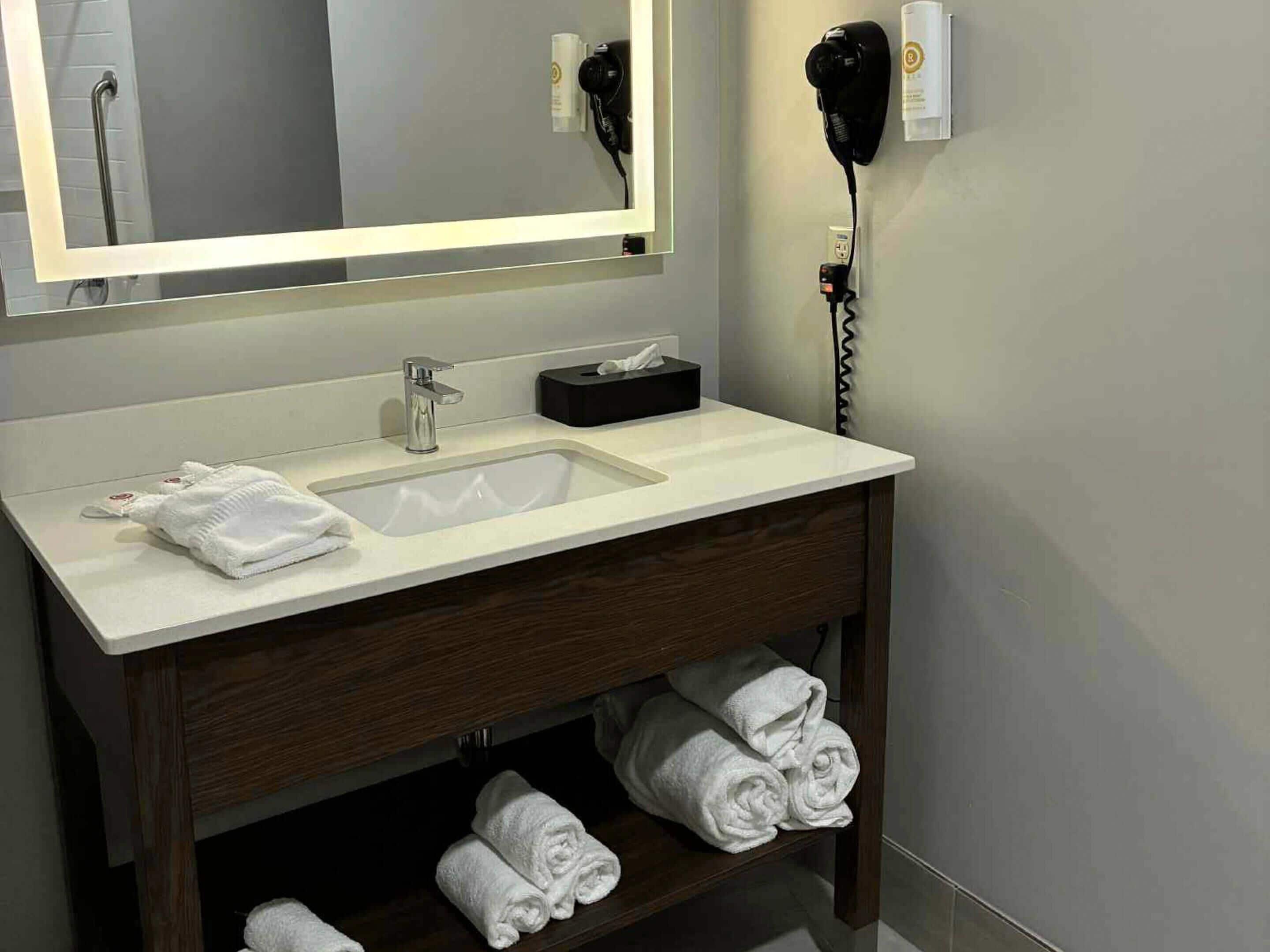 Uma casa de banho moderna com um espelho grande, uma pia, um porta-toalhas e um secador de cabelo.