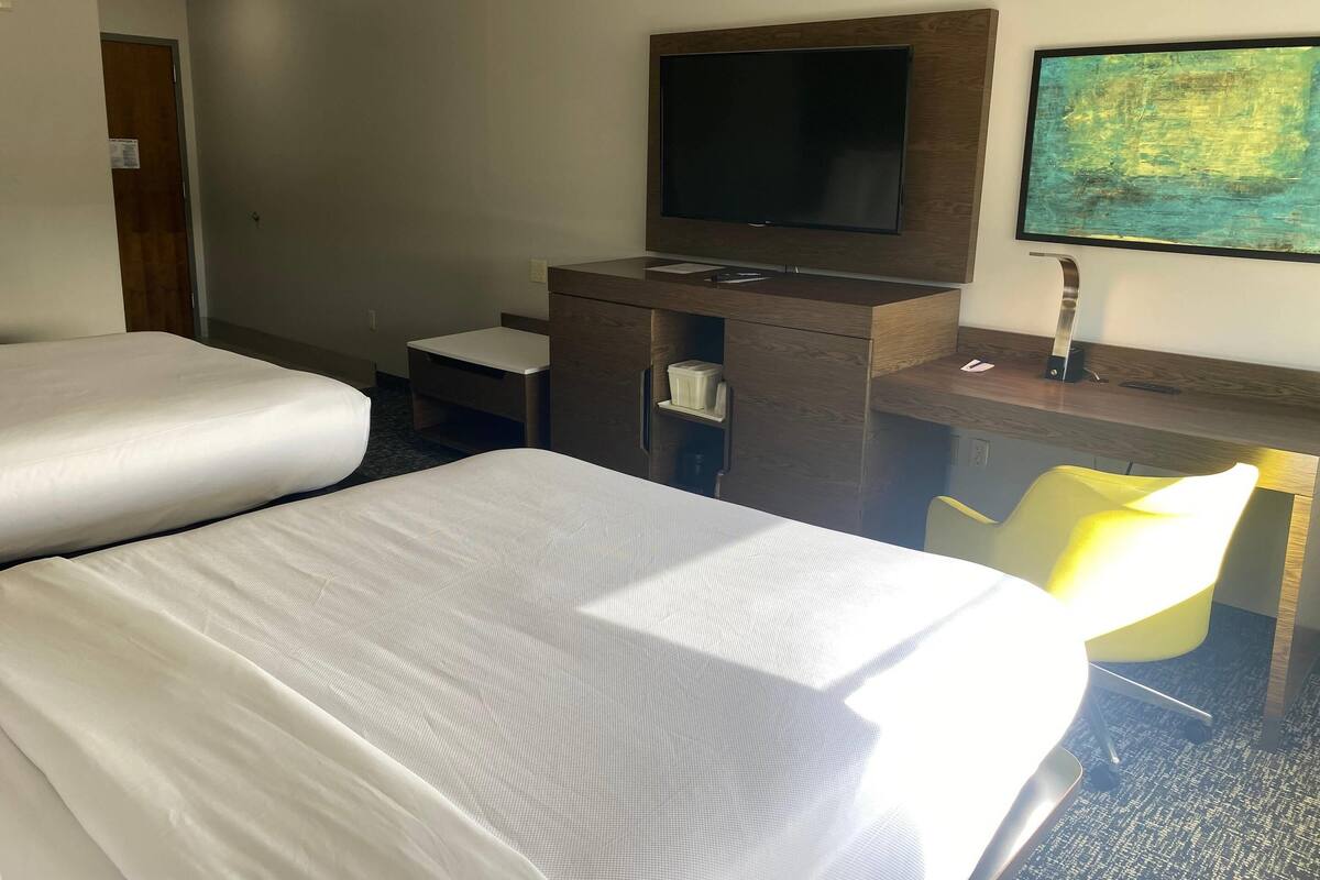 Een hotelkamer met twee bedden, een bureau met een flatscreen televisie, een stoel en een tafeltje.