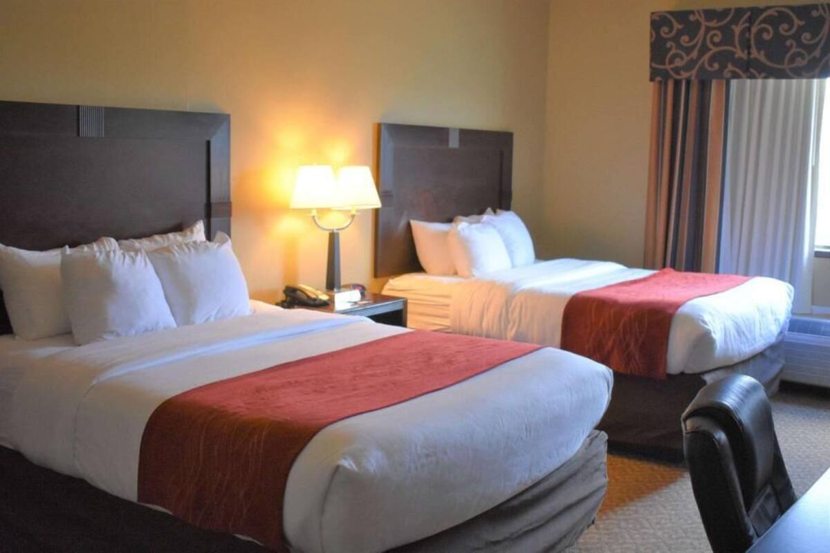 Een hotelkamer met twee bedden, een nachtkastje met lamp, een stoel en een raam met gordijnen.