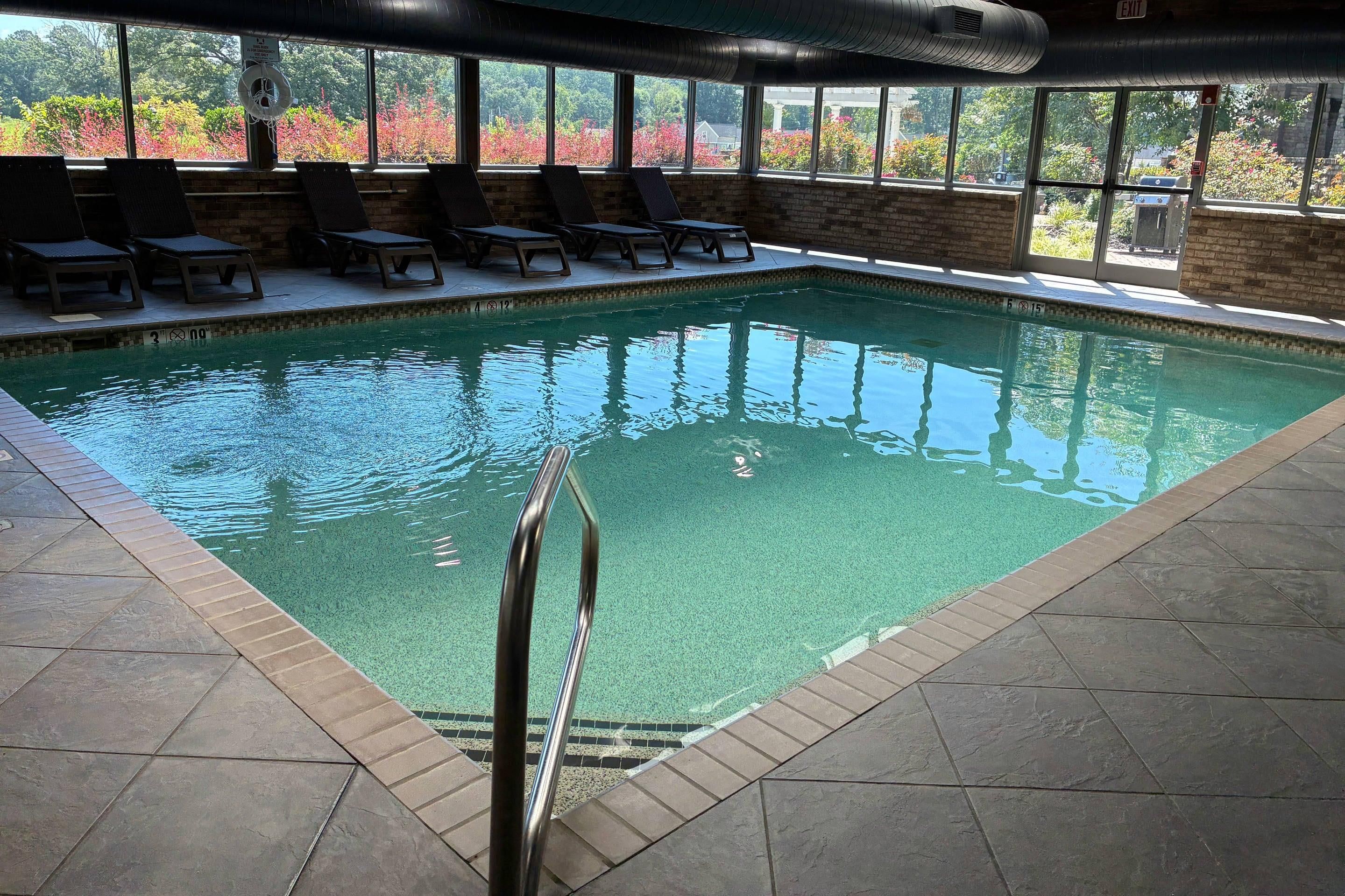 Una piscina interior con agua cristalina, rodeada de sillones de descanso y un muro de ladrillo.