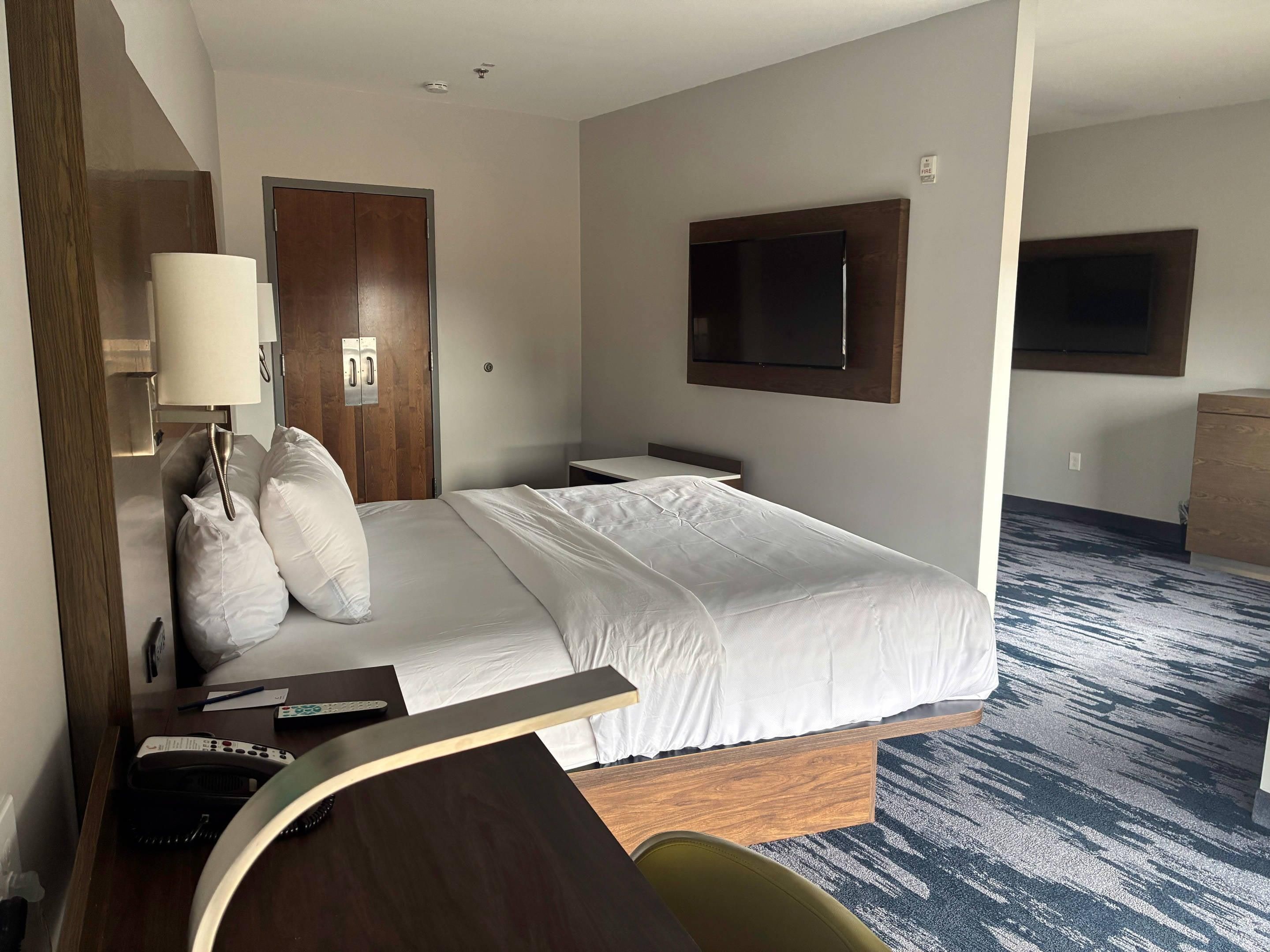 Ein Hotelzimmer mit Bett, Schreibtisch, Stuhl, Fernseher und einer Tür.