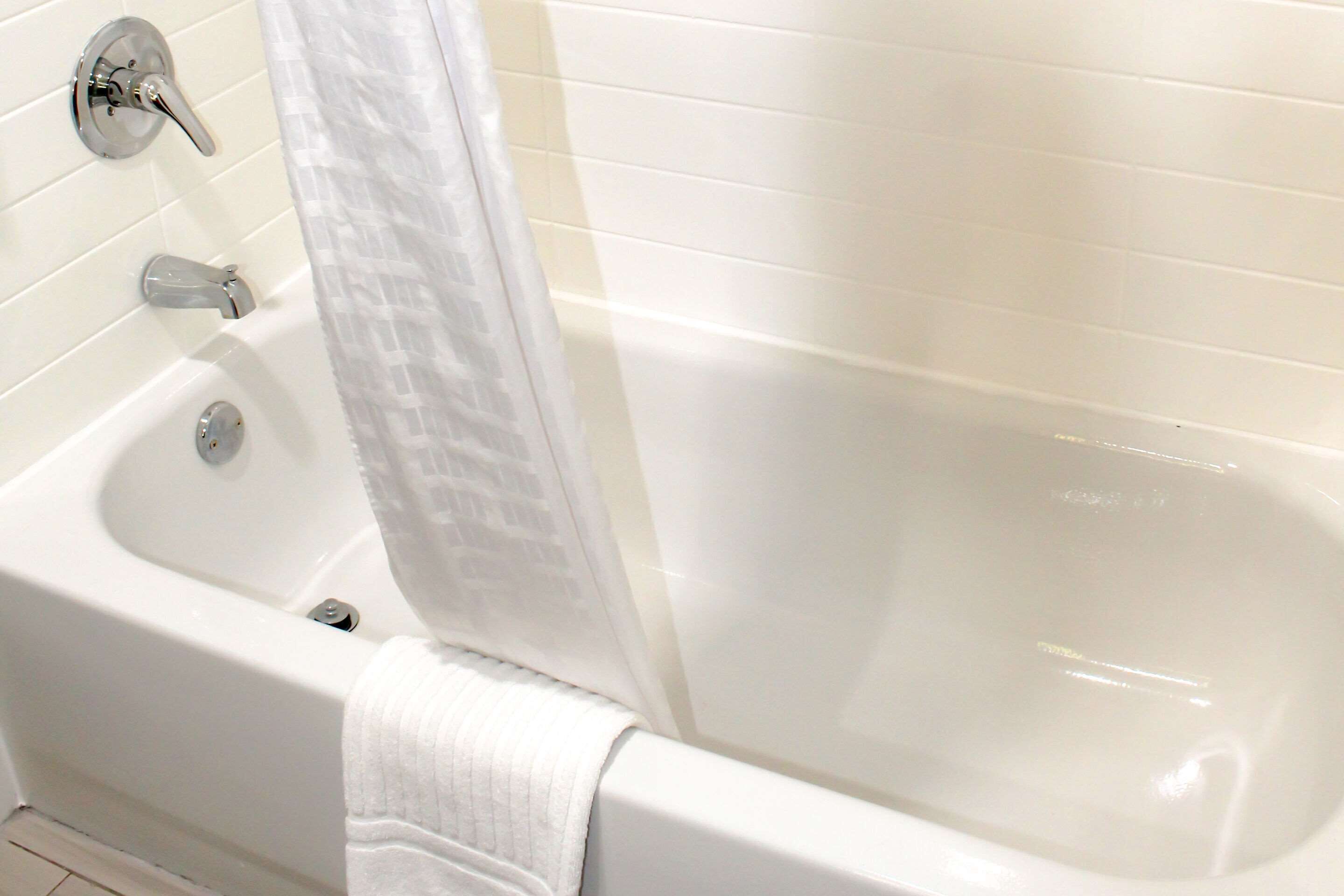 A bathtub with a shower curtain, a faucet, and a drain.
