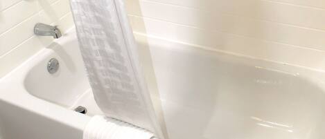A bathtub with a shower curtain, a faucet, and a drain.