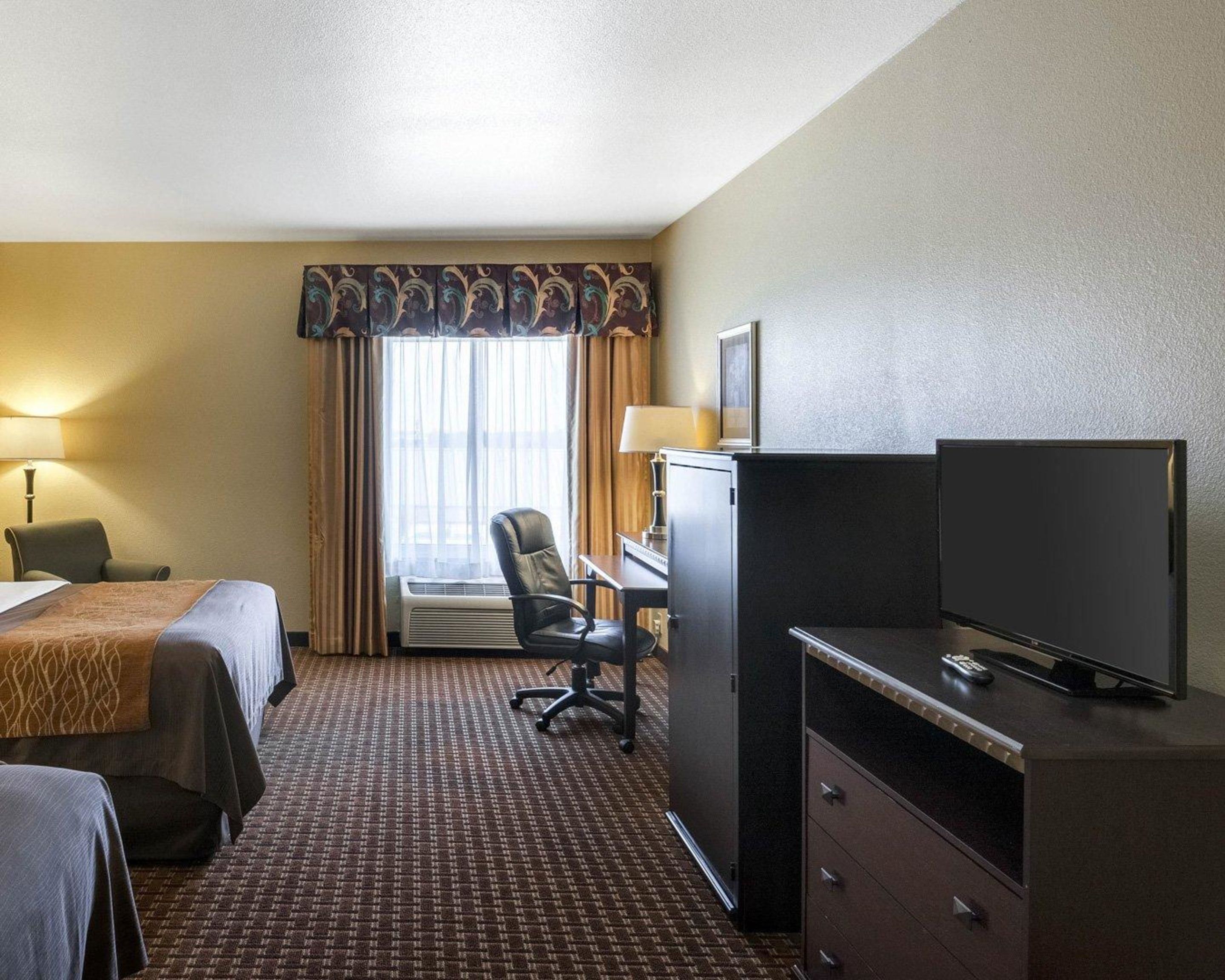 A hotel room with two beds, a desk, a chair, a television, and a window with curtains.