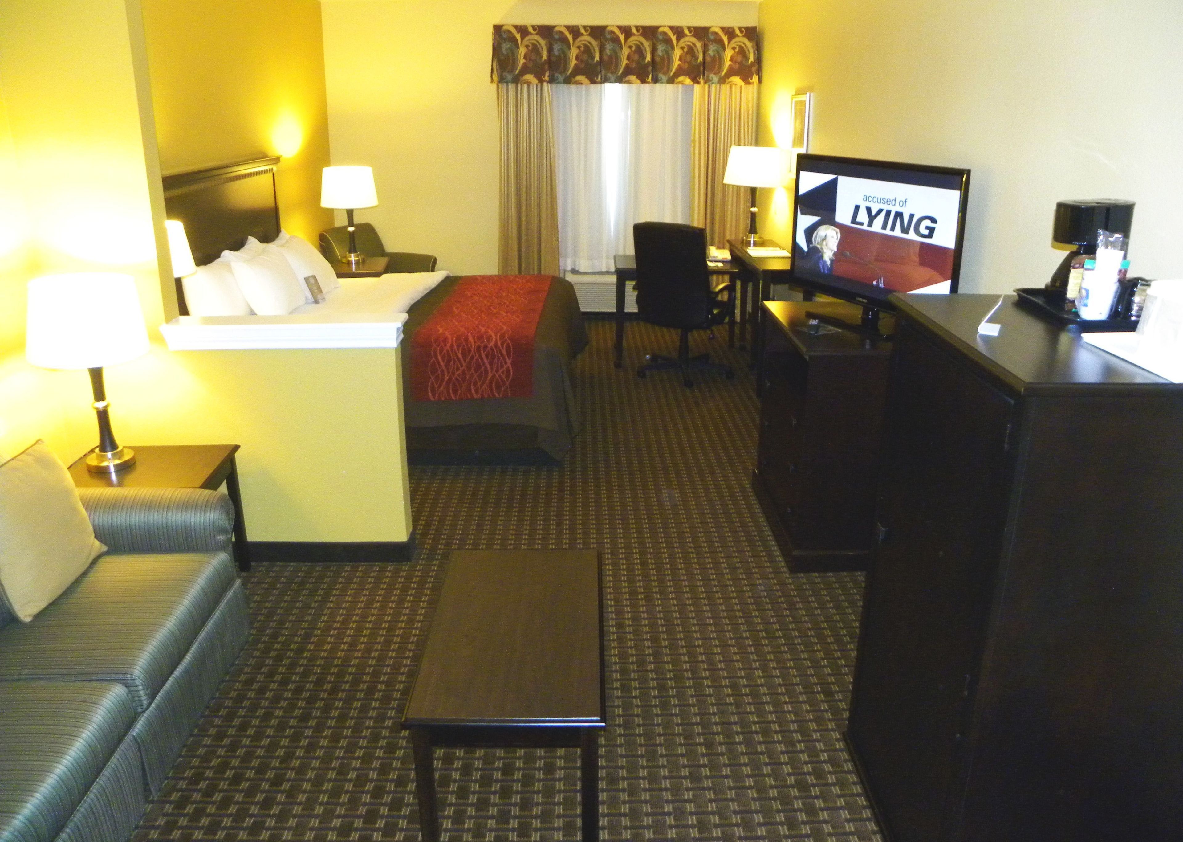 A hotel room with a bed, a sofa, a desk, a TV, and a coffee machine.