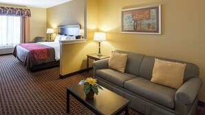 A hotel room with a bed, a sofa, a coffee table with a flower, a lamp, and a painting on the wall. - Comfort Inn & Suites Regional Medical Center (Abilene)