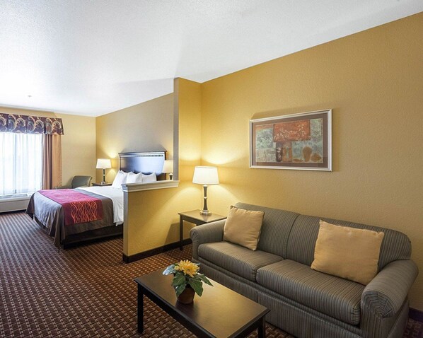 A hotel room with a bed, a sofa, a coffee table with a flower, a lamp, and a painting on the wall. - Comfort Inn & Suites Regional Medical Center (Abilene)
